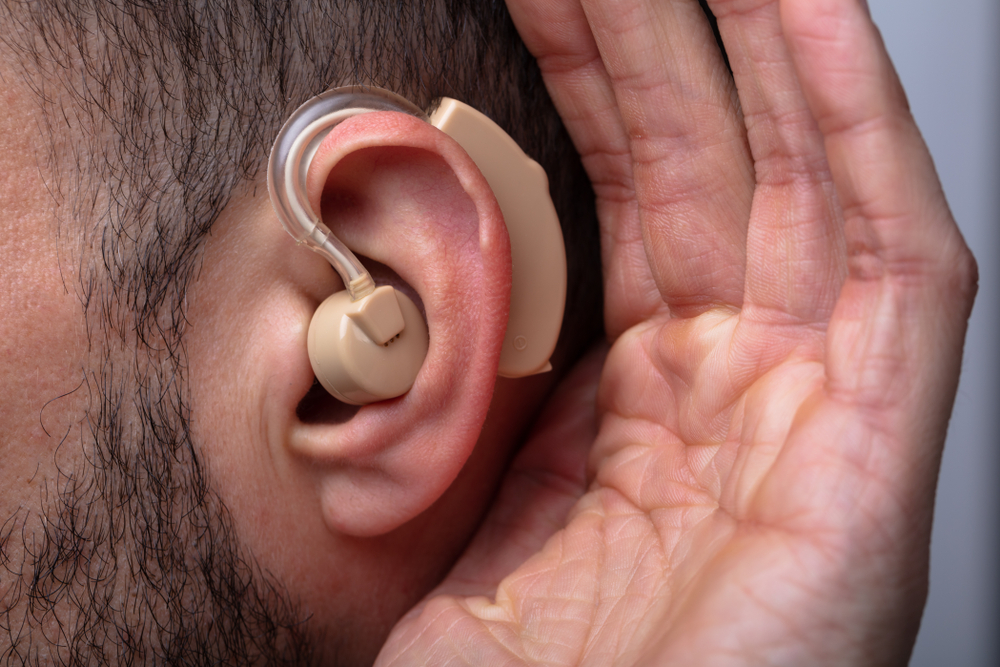 Man with short hair and beard putting hand to ear with hearing aid